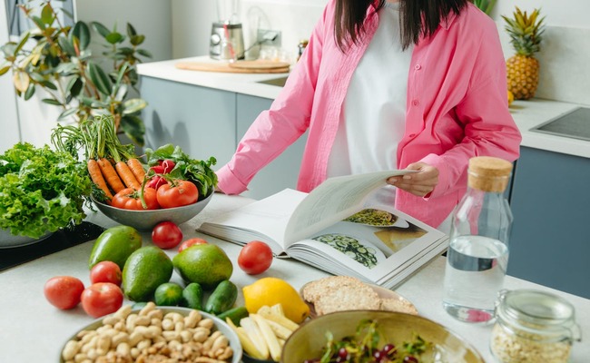 A lady in the kitchen reading a recipe book, looking for a essential holistic meal plan.