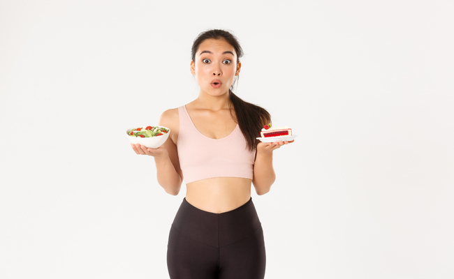 2. A person looking indecisive while holding a nutritious salad in one hand and a tempting slice of cake in the other, highlighting the considerations for pre-workout food choices.