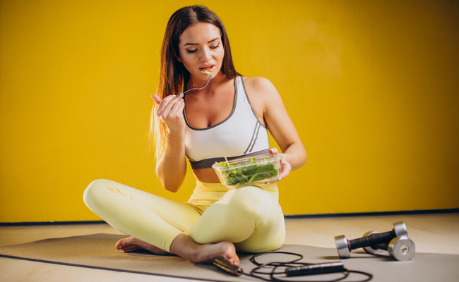 A woman is shown eating a salad before a workout, emphasizing the role of fresh, healthy food in fueling physical activity and recovery.